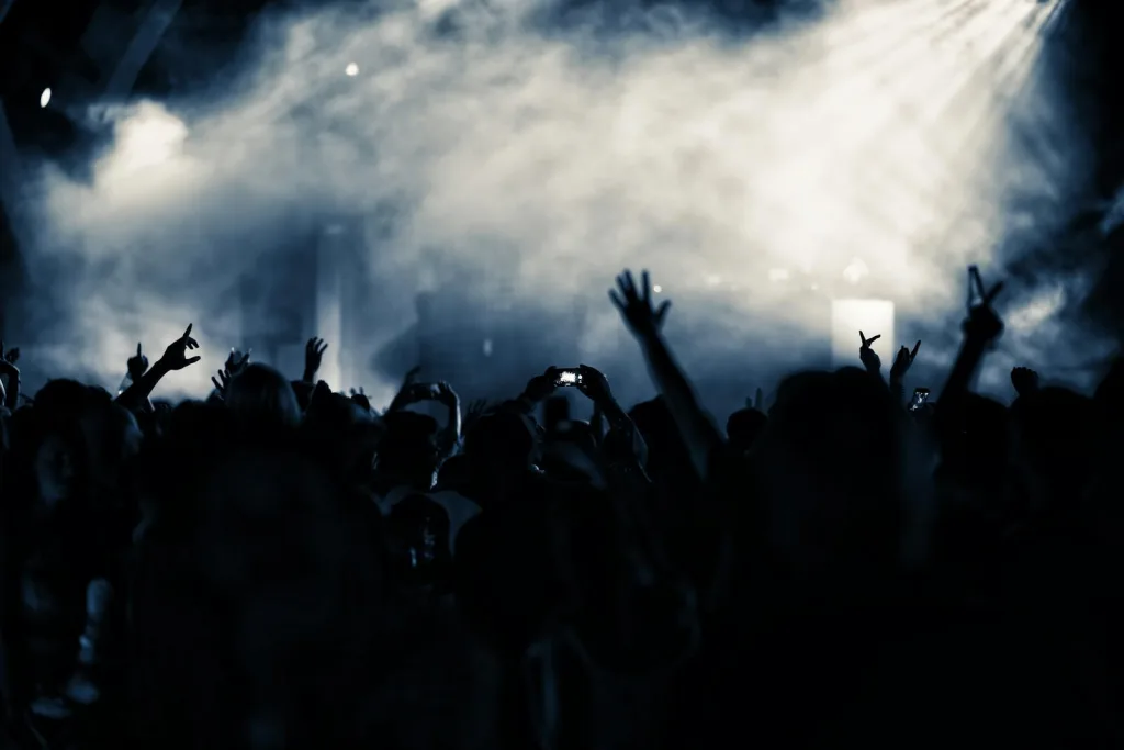 A lively nightclub concert scene with a cheering crowd illuminated by blue lights.